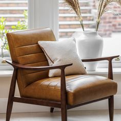 a brown leather chair sitting in front of a white vase and window with flowers on it