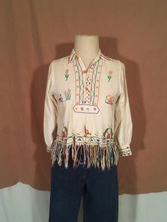 "1949 handmade souvenir blouse one of a kind pull over collared button up neck fringe hem cross stitch embroidered flowers, birds, people, elephants, bunnies good vintage condition, light wear cotton measures, lying flat, shoulder-13 1/2\" chest-18 1/2\" sleeve-18 1/2\" length-18 1/2\" length w/fringe-23\"" Traditional Cream Long Sleeve Top, Traditional Long Sleeve Cream Top, Vintage Cream Cotton Shirt, Cream Vintage Cotton Shirt, Vintage Cotton Shirt For Festivals, Vintage Embroidered Tops For Fall, Vintage Cream Tops With Floral Embroidery, Vintage Cream Top With Floral Embroidery, Vintage Cream Cotton Top