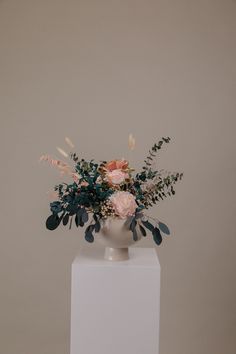 a vase filled with flowers on top of a white pedestal next to a gray wall