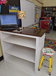 a laptop computer sitting on top of a white shelf in a classroom next to a yellow stool