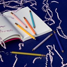 an open notebook and several pencils on a blue surface