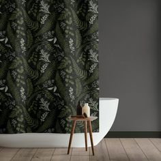 a bath tub sitting next to a shower curtain with leaves on it and a candle