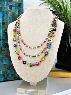 "I made this fun and colorful beaded necklace, with multi strands of glass seed beads, in a rainbow of colors. The larger glass beads on the longest strand, are made with multi colored evil eye beads, and multi colored millefiori beads. This necklace has 3 strands of colorful beads. Add color and get noticed, with this statement necklace for women who are fun and colorful. This colorful necklace is 24 inches long, and has a 2\" extension chain. This necklace is ready to send to you today, and in Colorful Fun Beaded Necklaces With Round Beads, Fun Multicolor Beaded Necklaces For Beach, Multicolor Round Beads Necklace - Fun Style, Handmade Multicolor Multi-strand Beads, Colorful Fun Round Beaded Necklaces, Multicolor Fun Beaded Necklace, Fun Multicolor Round Beads Necklace, Fun Multicolor Beaded Necklace, Fun Multicolor Handmade Beads