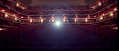 an empty theater with red seats and lights on the ceiling, looking down at the stage