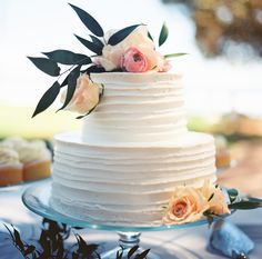 a white cake sitting on top of a table next to cupcakes and flowers