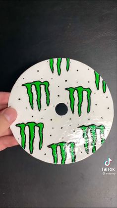 a hand holding a white and green disk with monster design on it's side