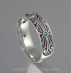 a wedding ring with an intricate design and green stones on the inside, in white gold