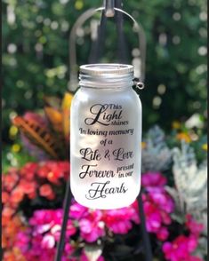 a mason jar hanging from a metal stand in front of flowers with words on it