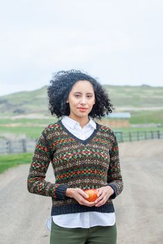 a woman holding an apple standing on a dirt road