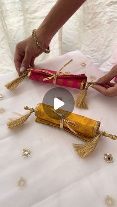 two people are making decorative items on a table with white cloth and gold tassels