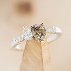 an engagement ring with two pear shaped diamonds on top of a piece of wood in front of a blurry background