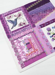 a close up of a quilt on a white surface with pink and purple squares in the center