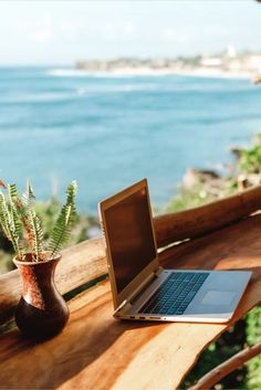 an open laptop computer sitting on top of a wooden table next to a potted plant