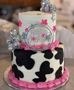 a birthday cake decorated with black and white cow print, pink ruffles and silver decorations