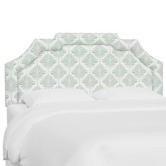 an upholstered headboard with white sheets and green palm leaves on the back