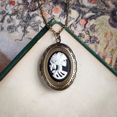 "Skeleton cameo on a vintage brass, antiqued, or shiny silver-plated oval locket, perfect for remembering your loved ones.  On 28 inches of chain. Choose your desired color.         I can change the chain to any length, just leave a note at checkout. Great for pictures of your loved ones.  Simply print, cut out, and attach a photo with glue.  We do not offer printer services at this time.  Fits a 17mm by 24mm oval photo. The box will include an oval stencil that will help you cut out your photo. Zombie Jewelry, Skeleton Jewelry, Skeleton Necklace, Cameo Bracelet, Pearl Charm Necklace, Picture Locket, Antique Locket, Picture Necklace, Oval Locket