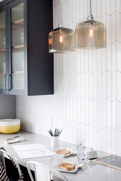 a kitchen table with two lights hanging over it and plates on the counter next to it