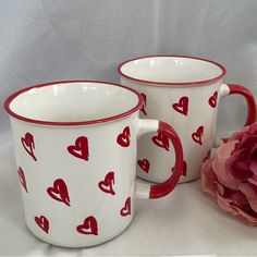 two red and white coffee mugs with hearts painted on them next to a pink flower