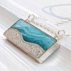 a silver and blue necklace on a white surface with water in the ocean behind it