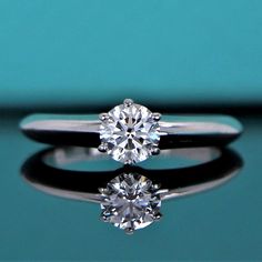 a diamond ring sitting on top of a blue surface with reflection in the glass table