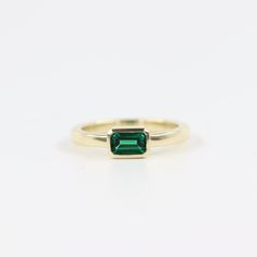 a gold ring with an emerald stone in the center and a thin band around it