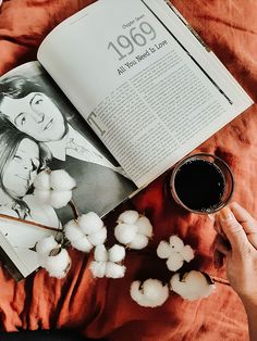 an open book with cotton floss next to it and a cup of coffee on the table