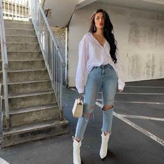 a woman standing in front of some stairs wearing ripped jeans and white boots with her hand on her hip