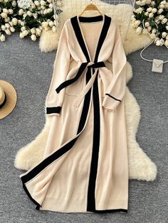 Tempt your fashion senses with this elegantly long cardigan, which combines a neutral beige hue with bold black detailing for a timeless piece. This garment's length and relaxed fit make it an ideal choice for those seeking both style and comfort. Weighing just 0.91 kg, it is light enough for all-day wear yet substantial enough to provide warmth. The cardigan's versatile design allows it to be worn open or cinched at the waist with its chic tie belt, adapting to both casual and formal settings. Beige V-neck Sweater Coat For Work, Elegant Spring V-neck Sweater Coat, Chic Beige Long Sleeve Cardigan, Elegant Beige Winter Cardigan, Elegant Beige V-neck Sweater Coat, Long Cream Sweater Coat For Spring, Elegant Beige V-neck Cardigan, Elegant Long Cream Cardigan, Elegant Cream Open Front Outerwear