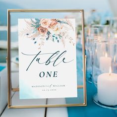 a close up of a sign on a table with candles in front of it and flowers