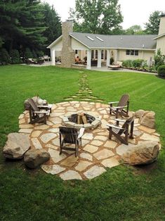 an outdoor fire pit surrounded by chairs in the middle of a grassy area with a house in the background