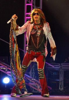 the man is performing on stage with his arms in the air while holding a snake