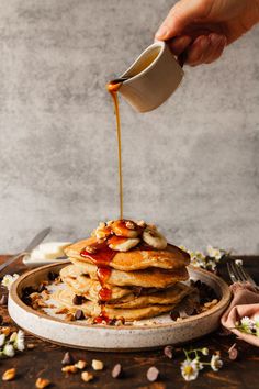 someone pouring syrup on top of a stack of pancakes