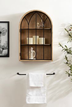 a shelf with candles and towels hanging on it next to a vase filled with flowers