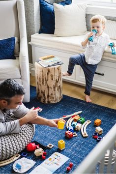 two children playing with toys on the floor in front of a white couch and window