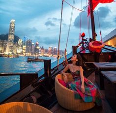 a woman sitting on top of a boat next to the cityscape at night