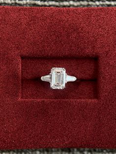 an emerald cut diamond ring in a red velvet display case on top of a carpeted surface