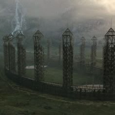 many metal structures in the middle of a grassy area with mountains in the background and foggy sky