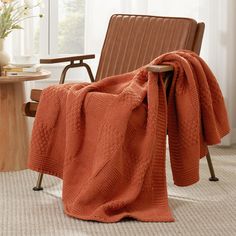 an orange knitted blanket sitting on top of a chair next to a vase with flowers