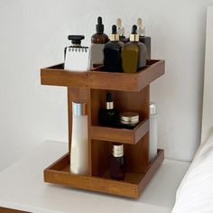 a wooden shelf with bottles and containers in it on a white table next to a bed