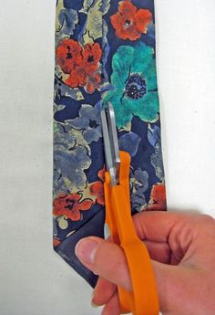 a person holding an orange pair of scissors in front of a tie with flowers on it