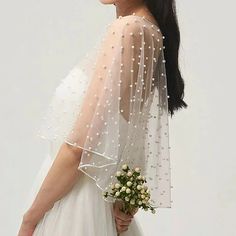 a woman wearing a wedding veil with pearls on the side and flowers in her hand