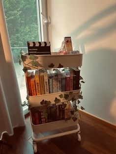 a bookshelf with many books on it in front of a window and wooden floor