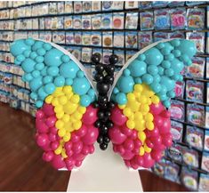 a colorful butterfly made out of balloons on a stand in front of a wall of cards