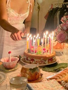 a woman is cutting into a cake with many lit candles on it and flowers in the background