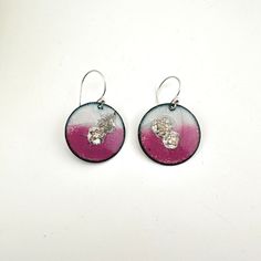 two round earrings with pink and white designs on them