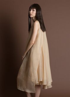 a woman standing in front of a brown background wearing a dress with an asymmetrical design