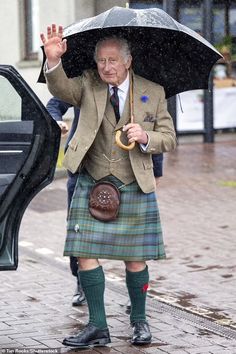 an old man wearing a kilt and holding an umbrella while walking in the rain