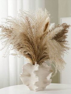 a white vase filled with dry grass on top of a table