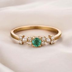 an emerald and pearl ring with three diamonds on the side, sitting on a white cloth