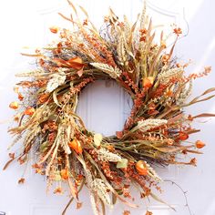 a wreath made out of dried flowers and leaves on the front door with an orange ribbon